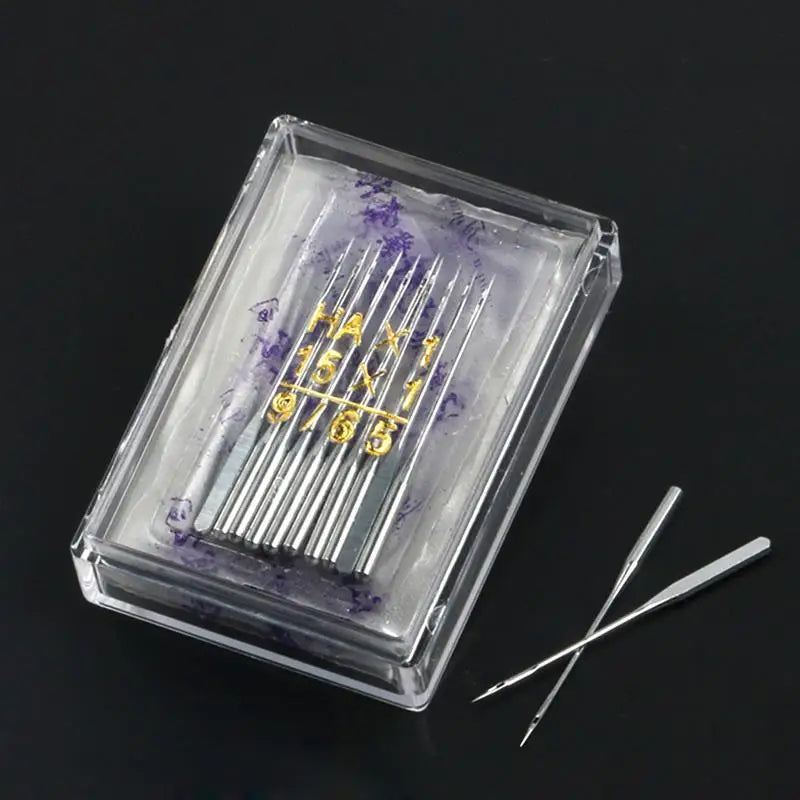 A clear plastic box containing a multi-pack of sewing machine needles with gold lettering on the packaging.