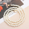 A strand of white pearls with gold clasps laid out on a light background.