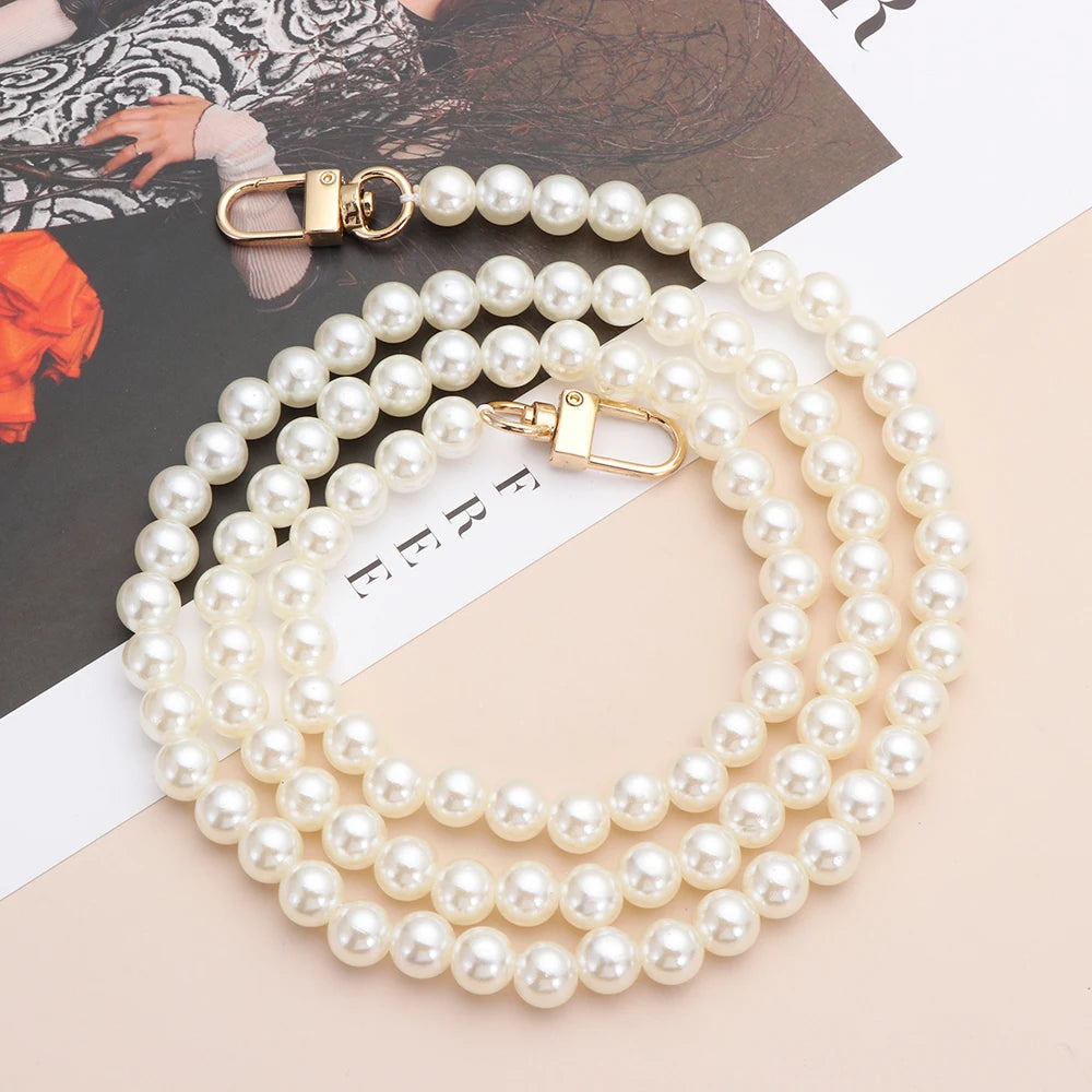 A strand of white pearls with gold clasps laid out on a light background.