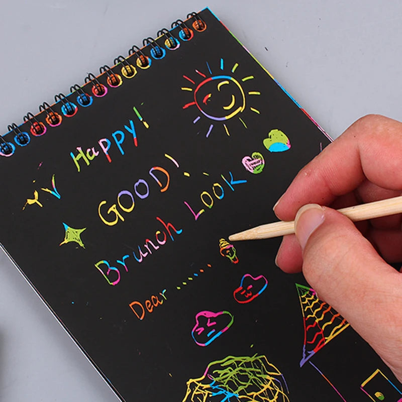 A hand writes 'Happy! Good! Brunch Look' on a black spiral notebook with colorful scratch art drawings.
