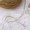 A spool of metallic gold silk crochet yarn with a loose strand draped over a white lace background.
