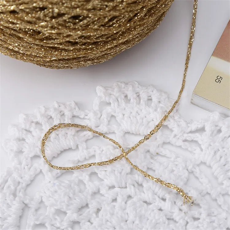 A spool of metallic gold silk crochet yarn with a loose strand draped over a white lace background.
