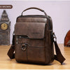 Dunkelbraune Vintage-PU-Leder-Crossbodytasche für Herren auf einer Holzoberfläche neben einer Standuhr.