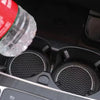 A clear glass bottle is shown next to a black non-slip cup mat designed for car interiors.