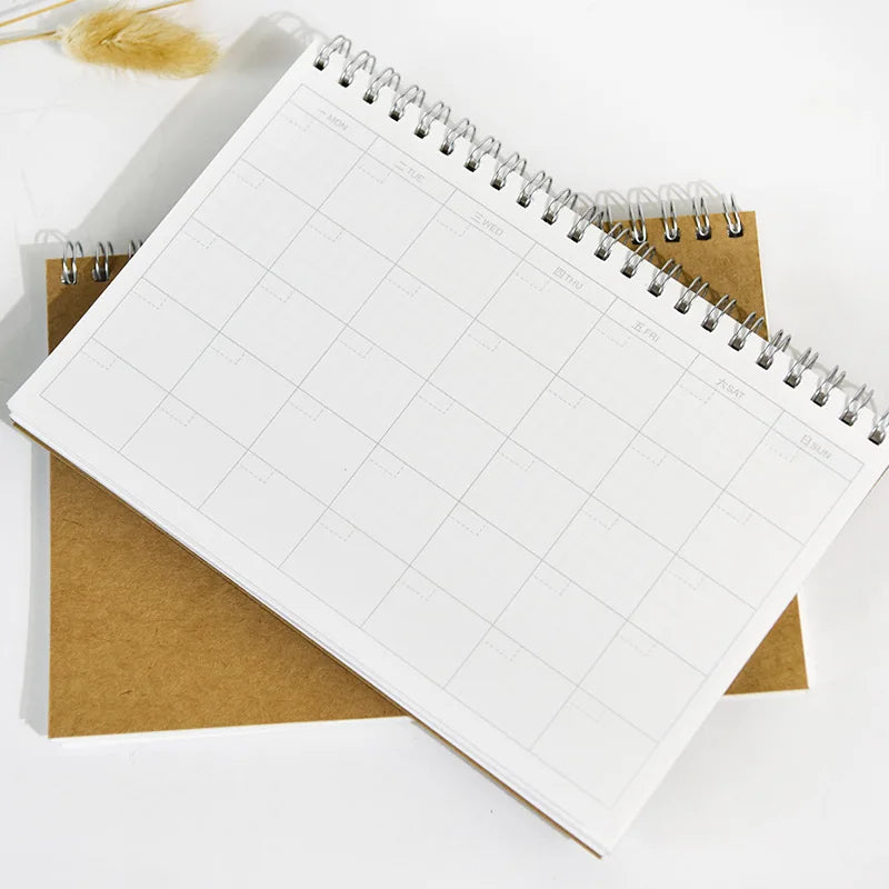 A spiral-bound monthly planner with a grid layout is shown on a brown background.