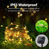A bundle of warm yellow fairy string lights is shown outdoors amidst green grass and raindrops, with a separate solar panel v