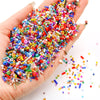 A hand holds a large pile of mixed glass seed beads in various colors and shapes for jewelry making