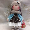 A handmade doll dressed in a gray knitted hat and blue coat with a polka dot skirt