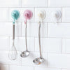Three kitchen utensils hanging on a white tile backsplash using suction cup hooks.