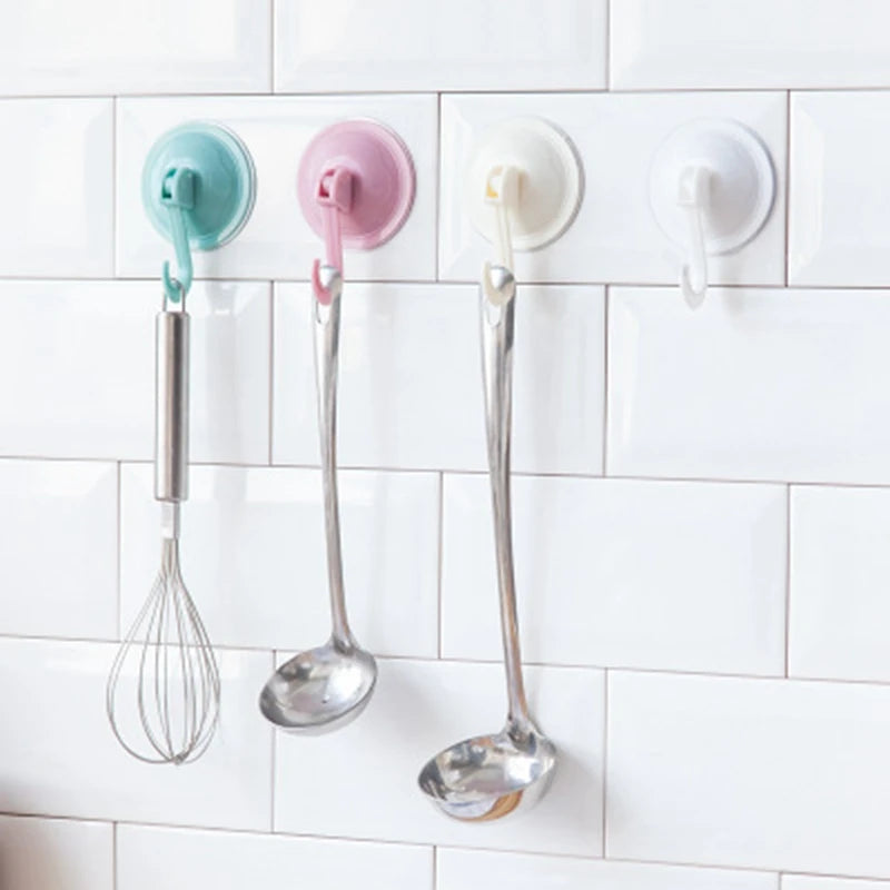 Three kitchen utensils hanging on a white tile backsplash using suction cup hooks.