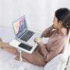 A woman is using an adjustable foldable laptop desk on a bed to work on a laptop.