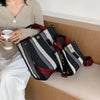 A woman holds a black and white striped canvas crossbody tote bag with red accents next to her.