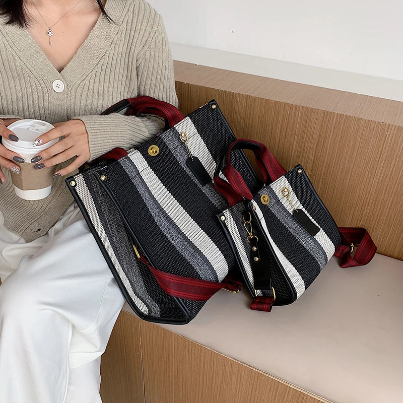A woman holds a black and white striped canvas crossbody tote bag with red accents next to her.