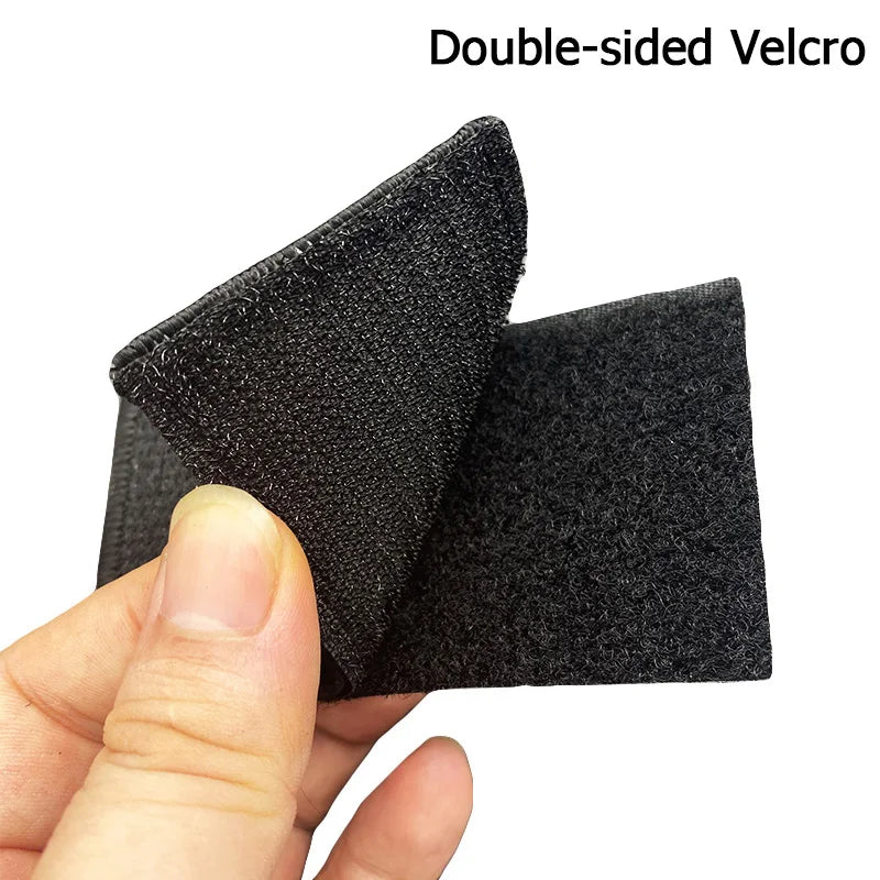 A hand holds a double-sided Velcro patch with black fabric and reflective accents.