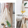 Two beige organic cotton mesh produce bags hanging on a wooden rack and being held by a person.