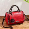A red leather crossbody shoulder bag with a floral pendant resting on a wooden surface.