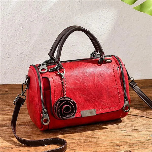 A red leather crossbody shoulder bag with a floral pendant resting on a wooden surface.