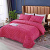 A pink quilted velvet bedspread with a ruffled edge is displayed on a bed in a bedroom setting.