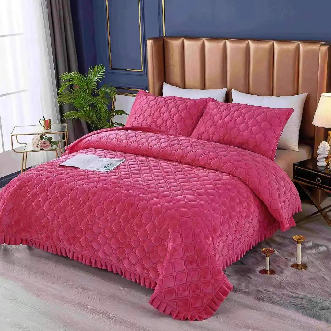 A pink quilted velvet bedspread with a ruffled edge is displayed on a bed in a bedroom setting.