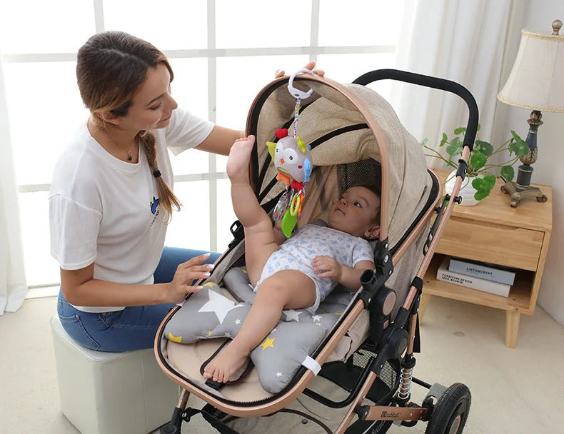A woman holds a soft plush baby rattle toy with a hanging bell and cartoon animal mobile in a stroller.