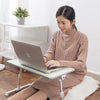A woman is using an adjustable foldable laptop desk while lying down on a wooden floor.