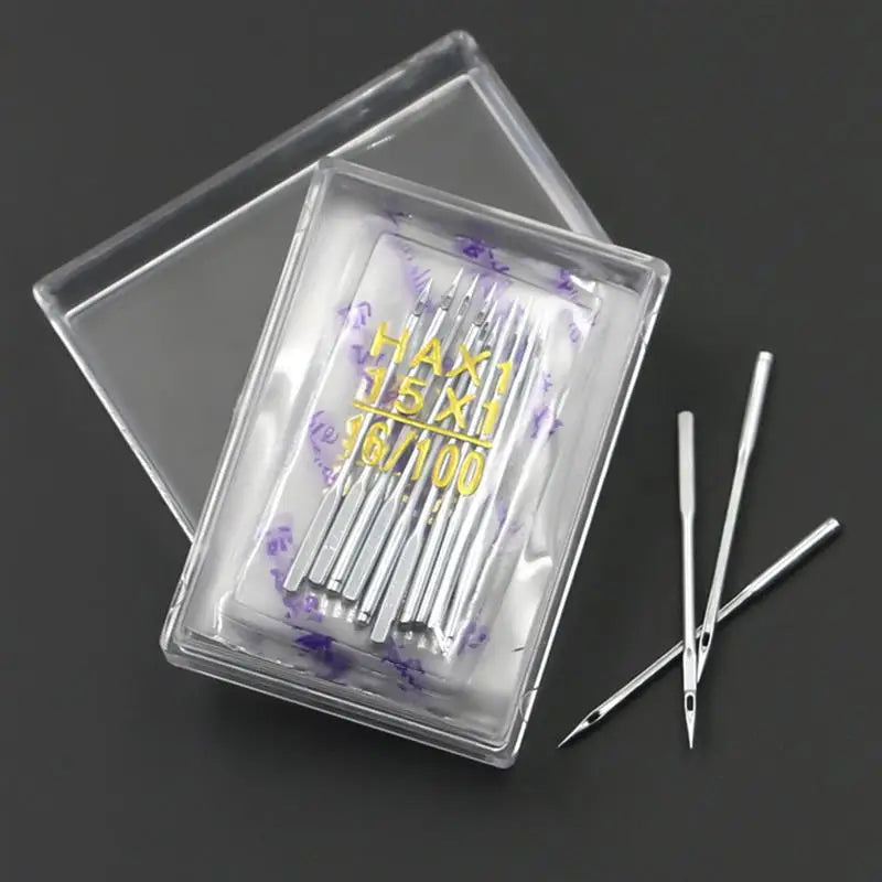 A clear plastic box containing a multi-pack of sewing machine needles with markings like HAX1 15x1 and 1/100.