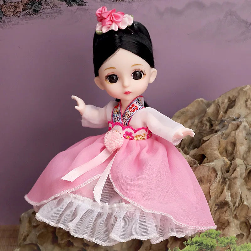 A pink fashion doll with black hair and a layered white and pink dress standing in front of a rocky background.