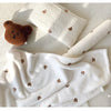 White coral fleece baby blanket with brown bear embroidery shown in various folds and textures.