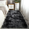 A black faux fur rug is displayed in front of a white bed and wooden cabinet.