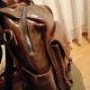 A close-up of a brown PU leather fashion backpack with a silver zipper and dark strap.