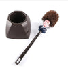 A novelty toilet brush with a figure head and bristles is shown next to its stand.