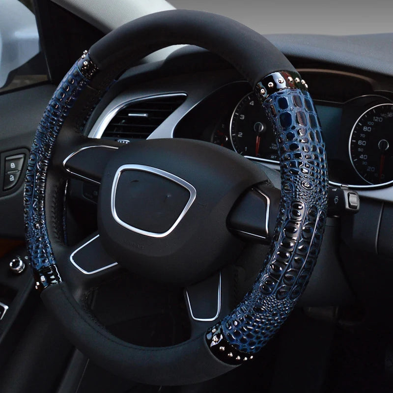 A close-up view of a black car steering wheel with blue crocodile grain leather covers.