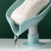 A leaf-shaped suction cup soap dish with a self-draining tray is shown dripping water onto a white surface.