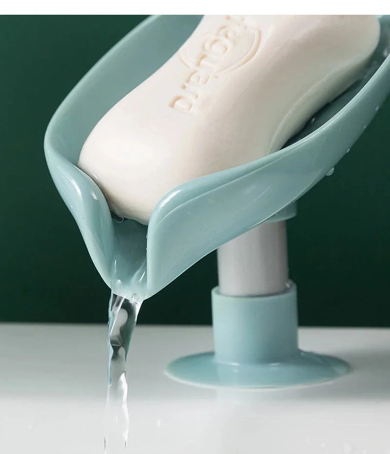 A leaf-shaped suction cup soap dish with a self-draining tray is shown dripping water onto a white surface.