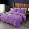 Purple quilted velvet bedspread with a diamond pattern on a bed in a bedroom setting.