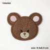 A brown felt animal patch of a bear face with pink ears and embroidered features.