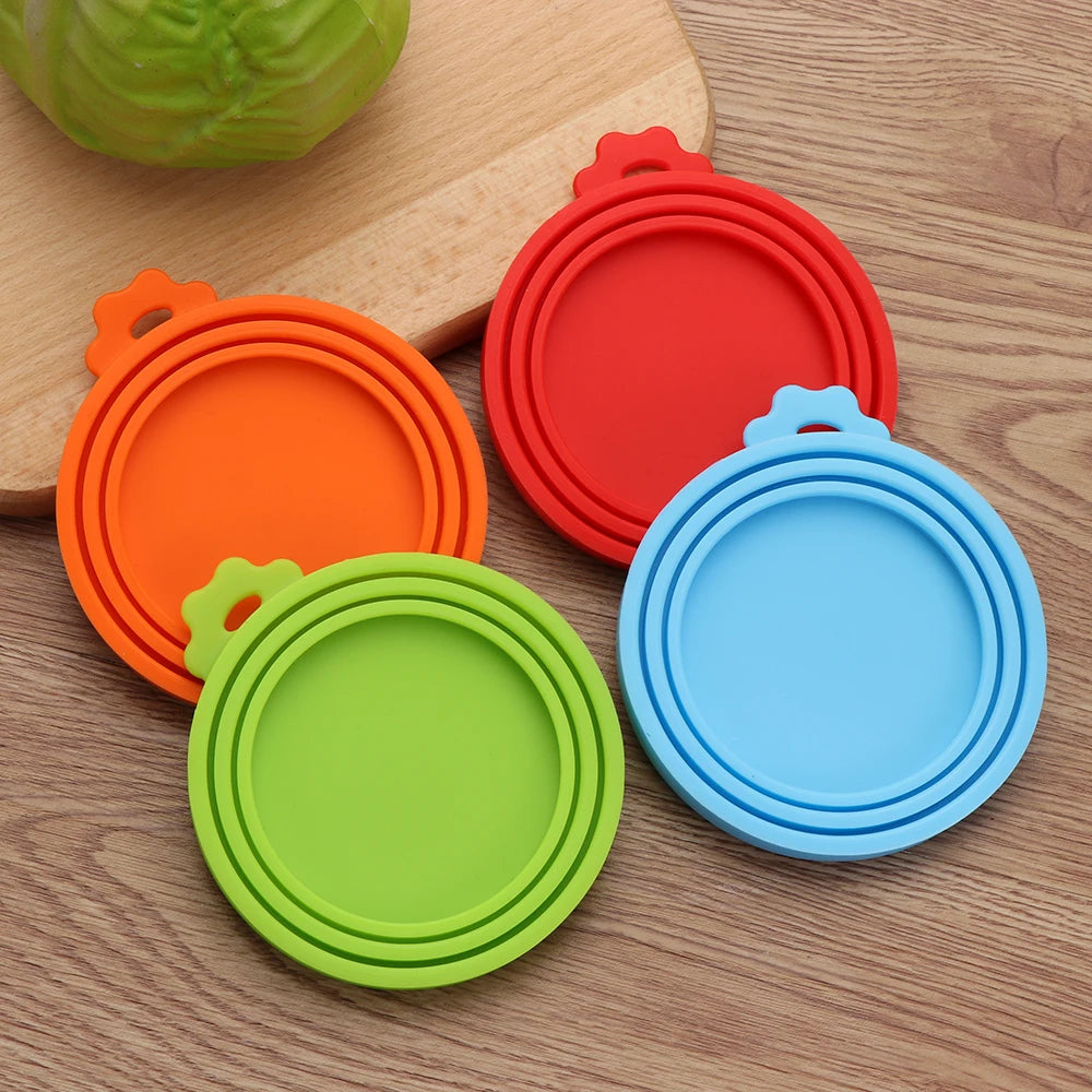 A set of three reusable silicone food storage lids in orange, red, and blue resting on a wooden surface.