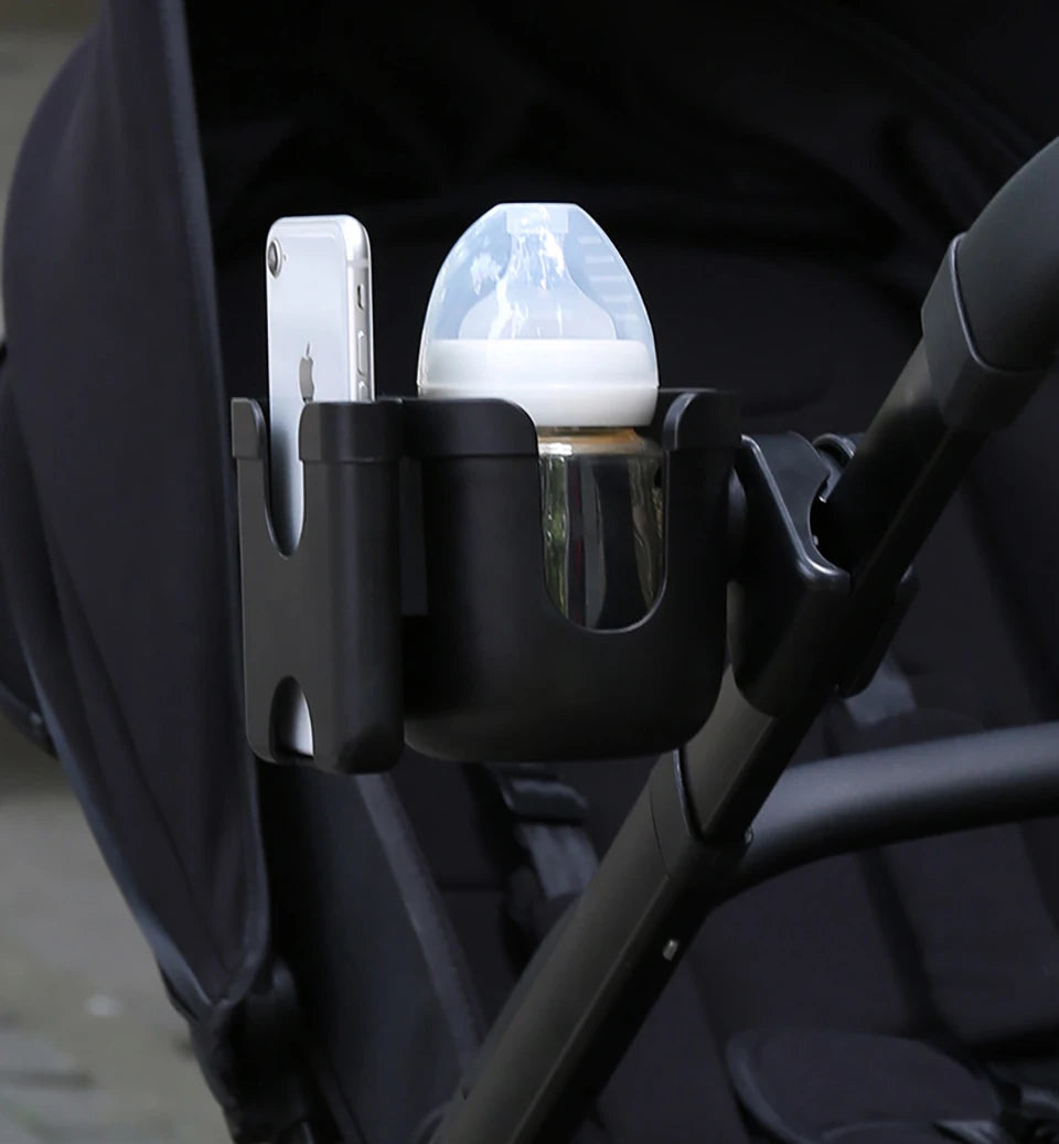 A black phone holder attaches to a stroller handlebar, holding an iPhone and a clear cup.