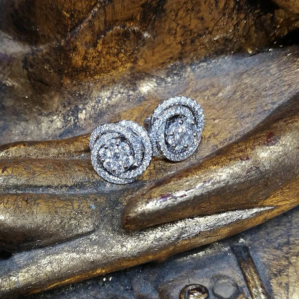 A pair of round geometric cubic zirconia stud earrings resting on a textured gold surface.
