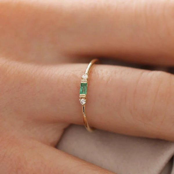 Gros plan d'une main portant une bague en or avec des accents de pierre verte.