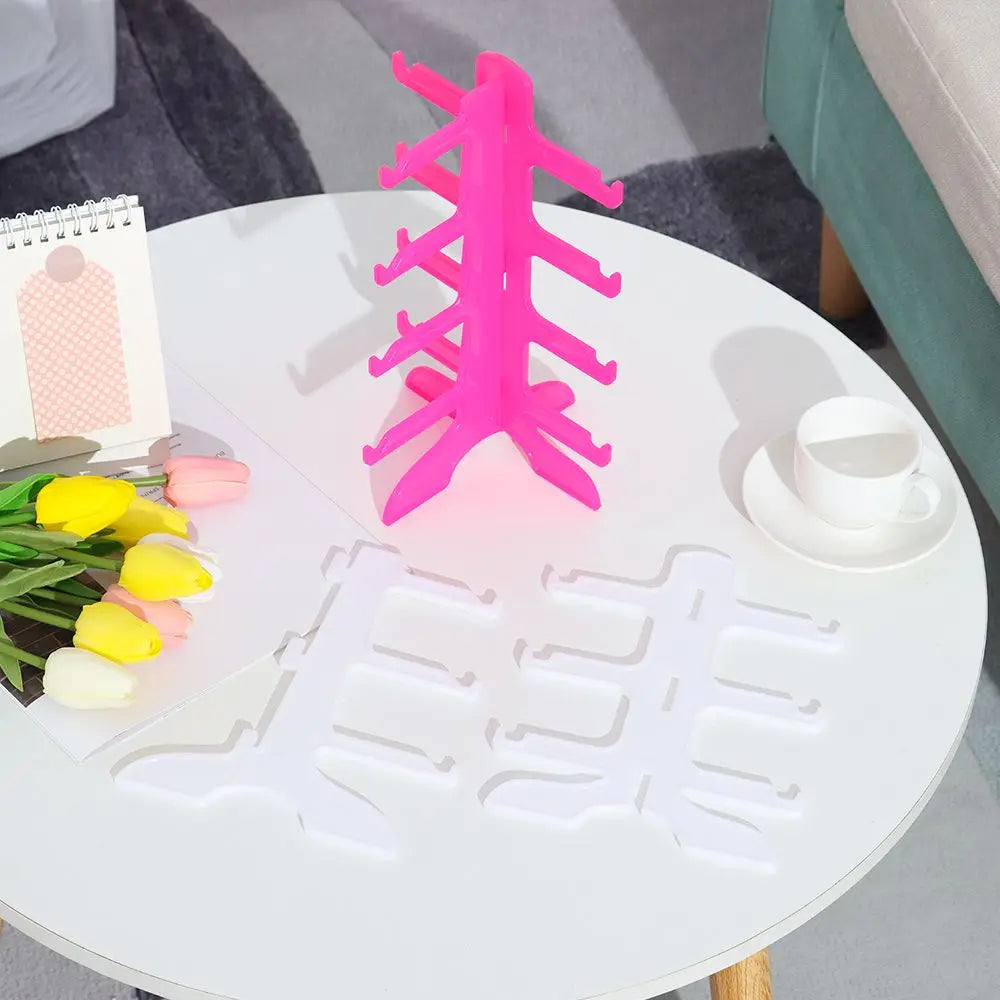 A bright pink acrylic stand shaped like a tree is displayed on a white table next to white eyeglass holders.