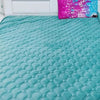A teal quilted velvet bedspread with a ruffled edge is displayed on a white bed with a headboard and a bright pink decorative