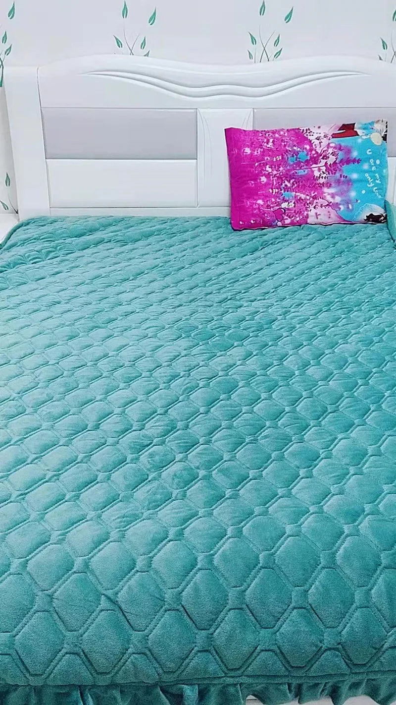 A teal quilted velvet bedspread with a ruffled edge is displayed on a white bed with a headboard and a bright pink decorative