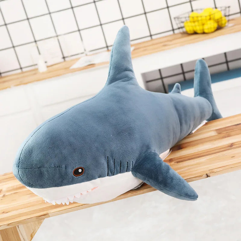 Ein weicher blau-weißer großer Haifisch-Plüschtier liegt auf einer Holzoberfläche.