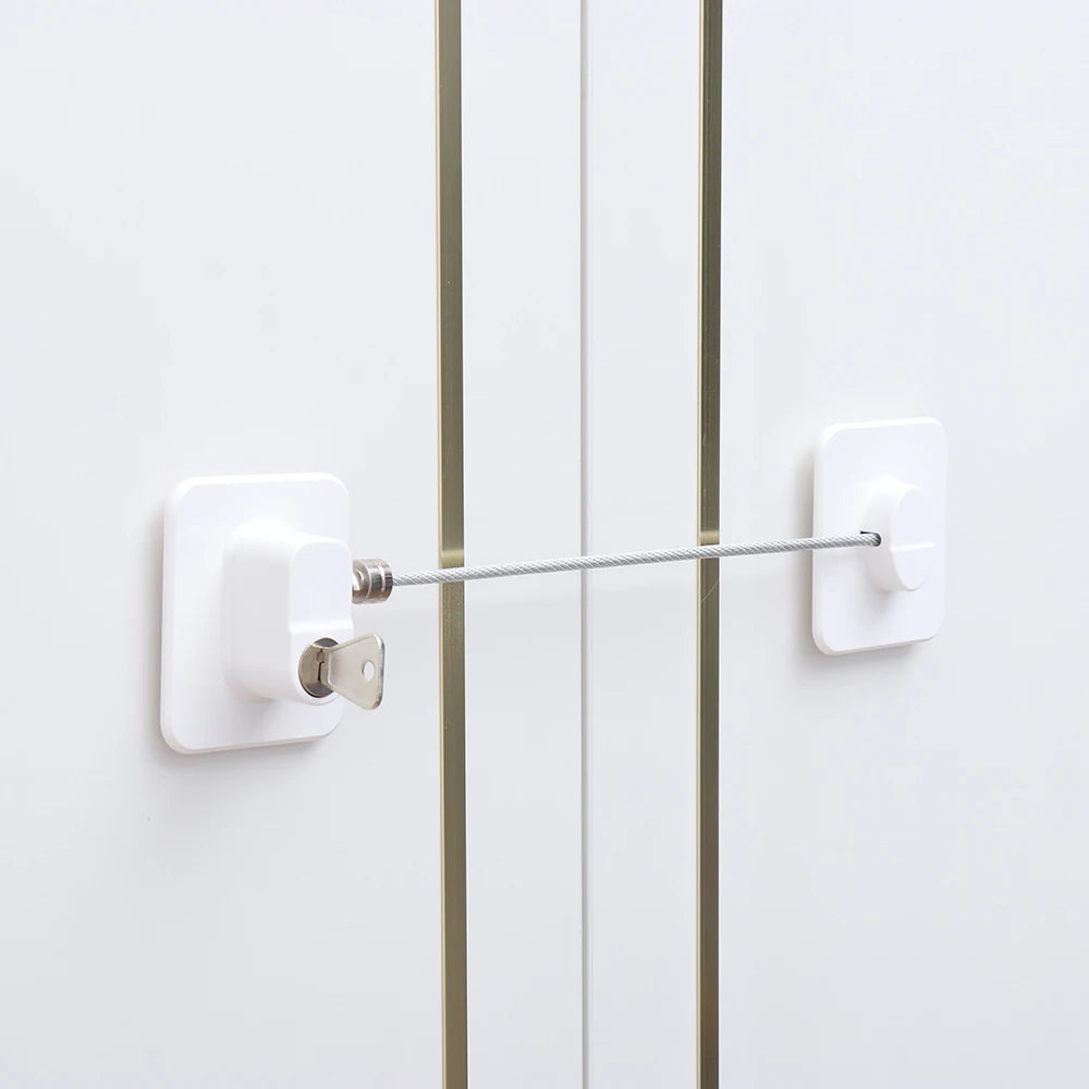 A white child safety cabinet lock with a key or digital code is mounted on a white door.