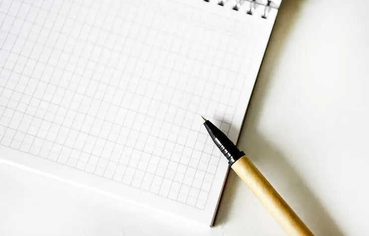 A close-up view of a spiral-bound monthly planner with blank grid pages and a wooden pen resting on the paper.