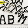 A collection of black embroidered alphabet patches, including YANANA and ABM, laid out on a white background with a ruler.