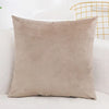 A square, light beige velvet decorative cushion cover resting on a white surface.