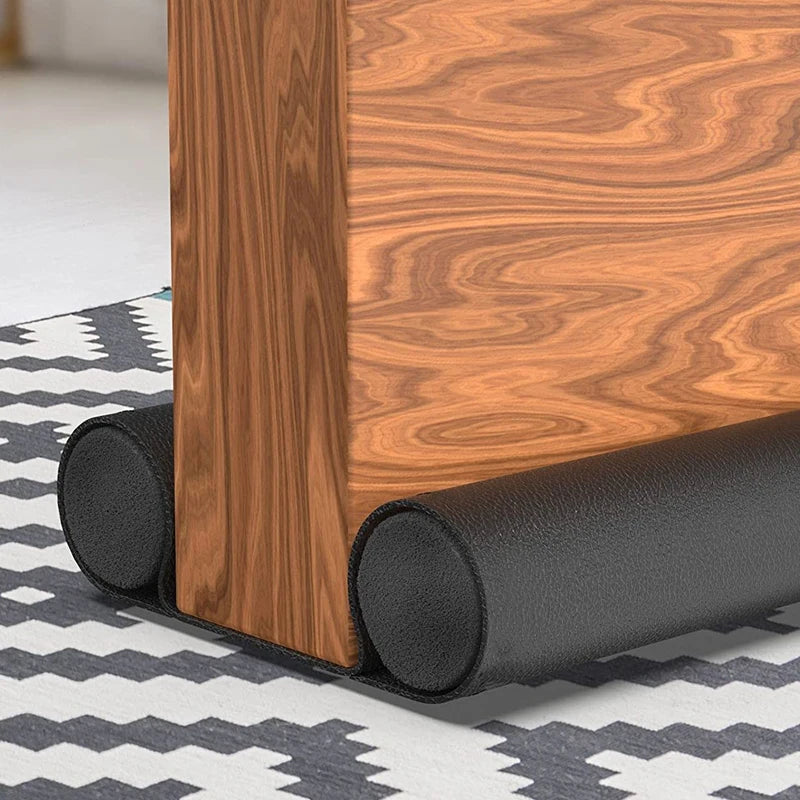 A close-up of a wooden door frame with a black flexible sealing strip installed at the bottom.