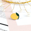 A gold wire fruit brooch pin featuring a yellow citrus fruit and green leaf, suspended by pearl-like beads.